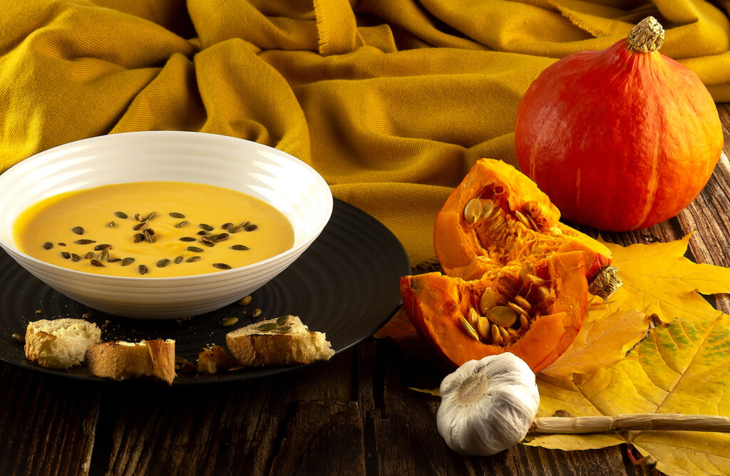 Pumpkin soup on a wooden table with other pumpkins