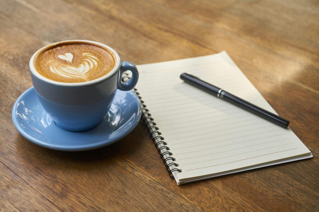 pexels-photo-414551-414551 A calming scene of a latte with art in a blue cup beside a notebook and pen on a wooden table.