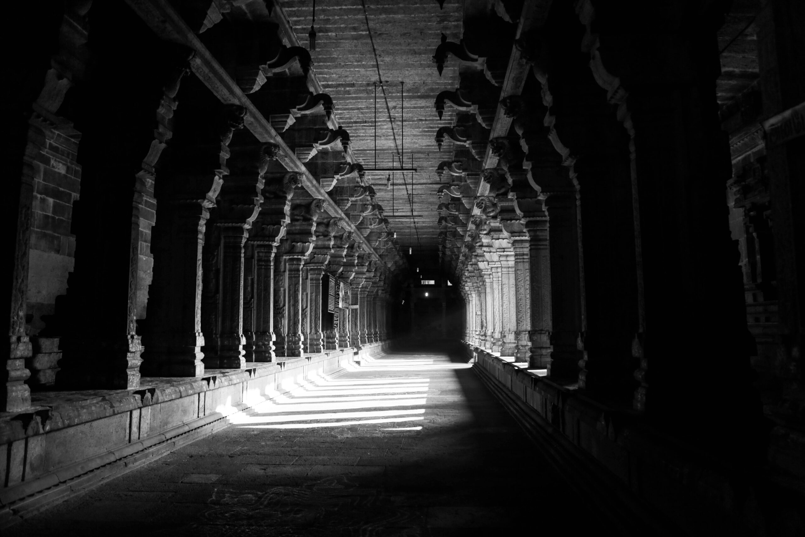 Monochrome image of an eerie temple hallway with dramatic light and shadow play.