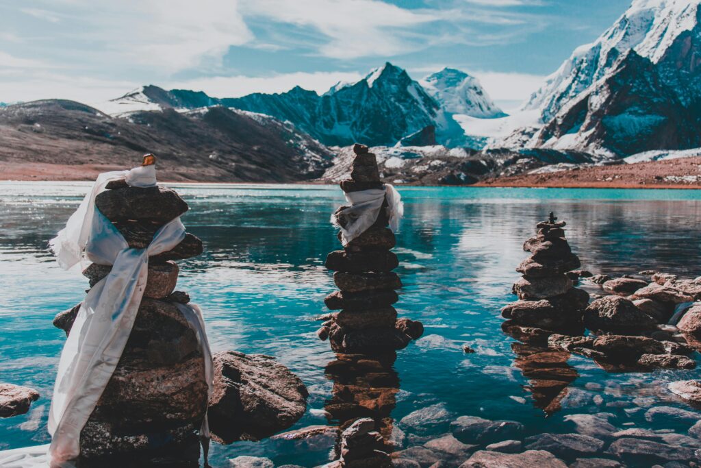 Calm lake scene with majestic snow-capped mountains and tranquil rock cairns.