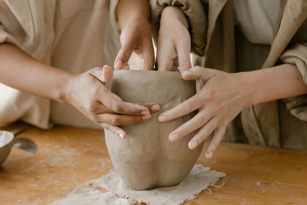Close-up of diverse hands shaping clay pottery on a wooden table, showcasing craftsmanship.