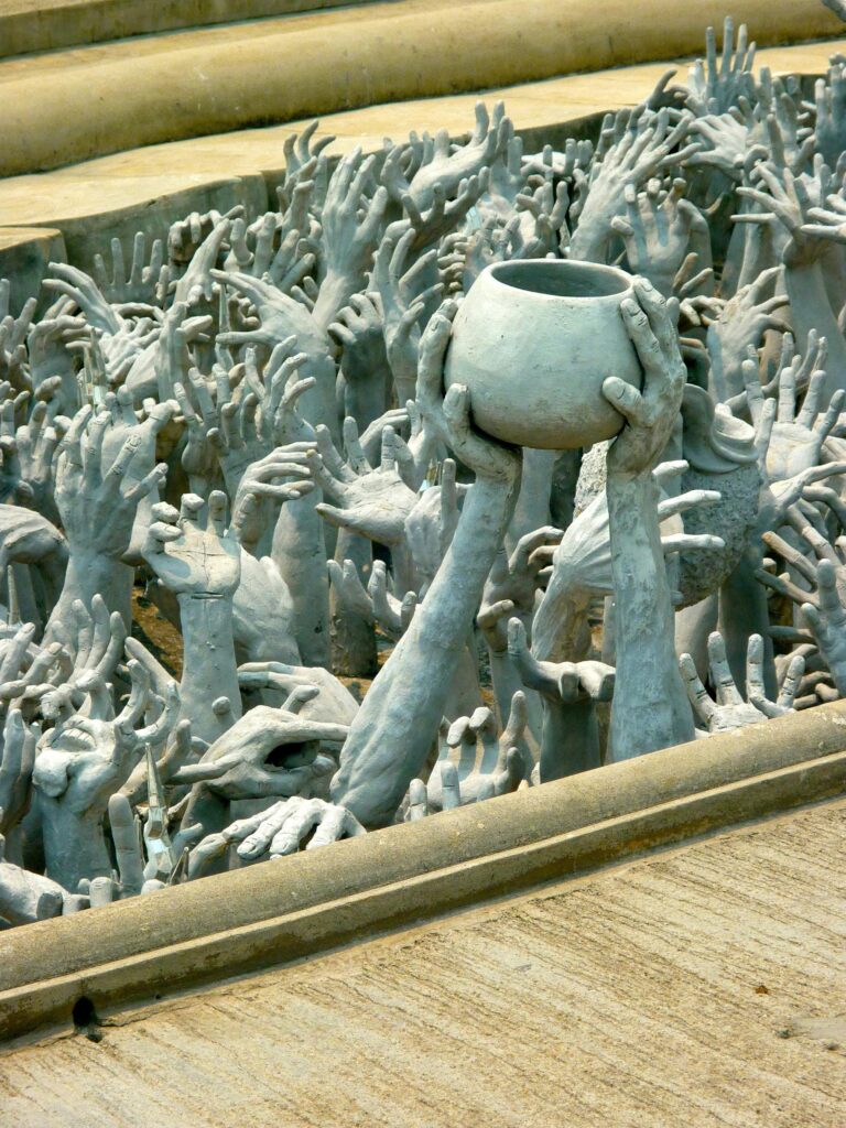 Intricate sculpture of hands reaching towards the sky at Wat Rong Khun, a unique white temple in Thailand.