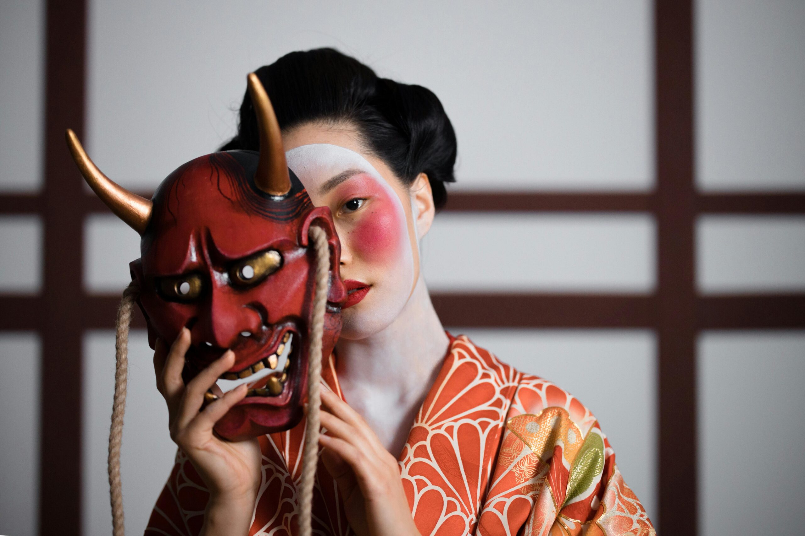 A geisha in a kimono holding a Hannya mask, symbolizing traditional Japanese culture.